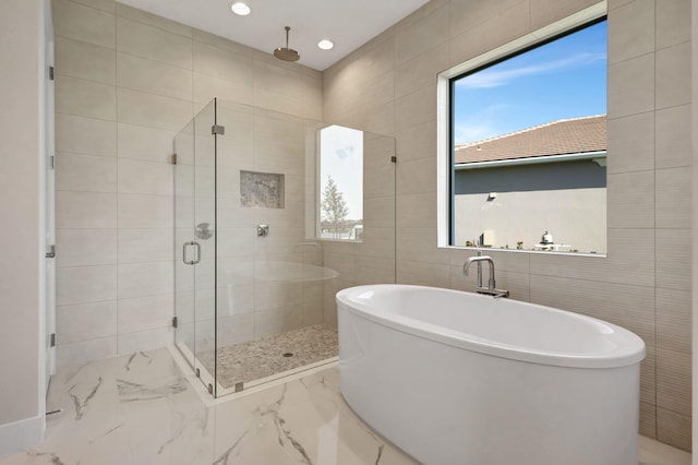 full bath with marble finish floor, a stall shower, a freestanding tub, and tile walls