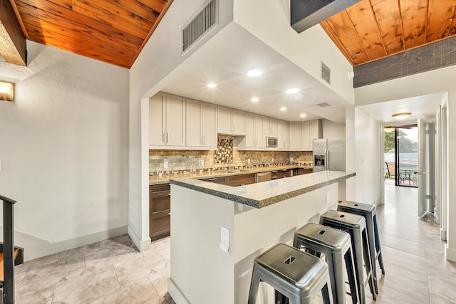 kitchen featuring a center island, wooden ceiling, a breakfast bar, decorative backsplash, and stainless steel appliances