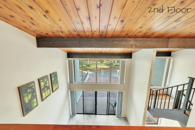 interior space featuring baseboards, wood ceiling, beam ceiling, and a high ceiling