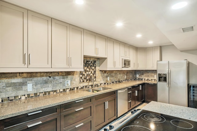 kitchen featuring a sink, stainless steel appliances, light stone counters, visible vents, and decorative backsplash