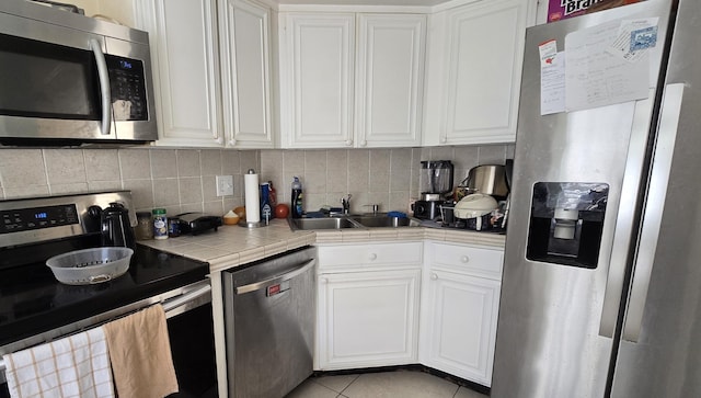 1823 Embassy Dr Unit 101, West Palm Beach, FL 33401 - kitchen featuring backsplash, a sink, tile counters, stainless steel appliances, and white cabinetry