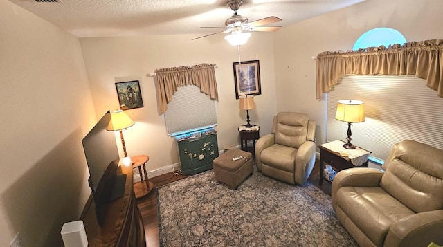 living room featuring a textured ceiling, ceiling fan, visible vents, baseboards, and wood finished floors