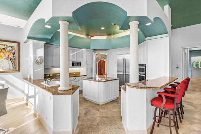 16330 Vintage Oaks Ln, Delray Beach, FL 33484 - kitchen with built in appliances, a peninsula, ornate columns, a towering ceiling, and a kitchen island