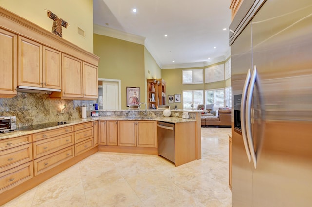 kitchen featuring light brown cabinetry, appliances with stainless steel finishes, a sink, a peninsula, and a towering ceiling