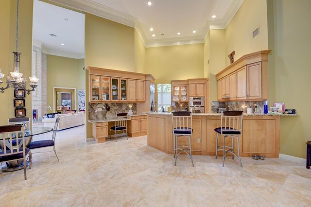 kitchen featuring an inviting chandelier, a towering ceiling, light brown cabinetry, and glass insert cabinets
