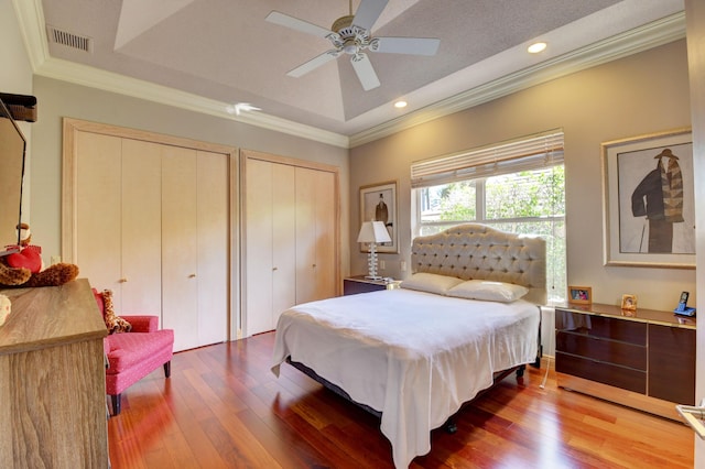 bedroom featuring visible vents, crown molding, multiple closets, wood-type flooring, and a tray ceiling
