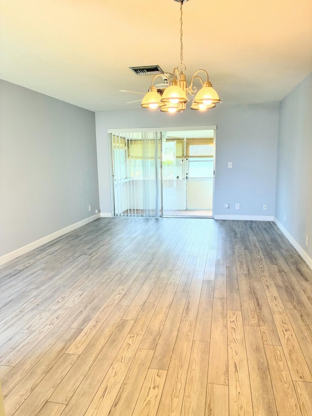 empty room featuring baseboards, an inviting chandelier, visible vents, and light wood-style floors