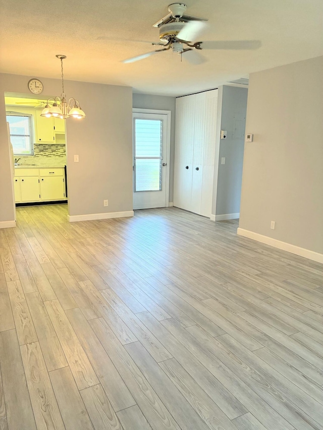 unfurnished living room with baseboards and ceiling fan with notable chandelier
