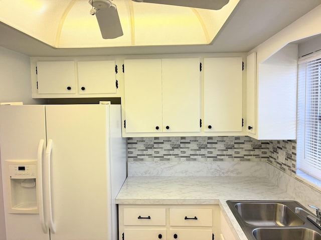 kitchen with a sink, light countertops, white refrigerator with ice dispenser, and backsplash