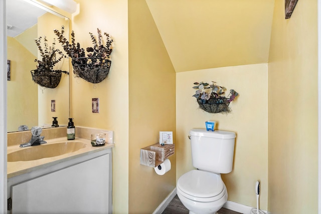 bathroom featuring wood finished floors, vanity, baseboards, toilet, and lofted ceiling