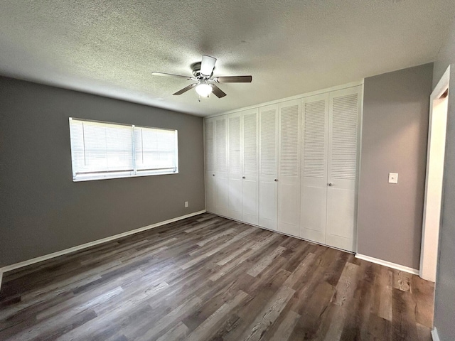 unfurnished bedroom with a textured ceiling, a ceiling fan, baseboards, wood finished floors, and a closet
