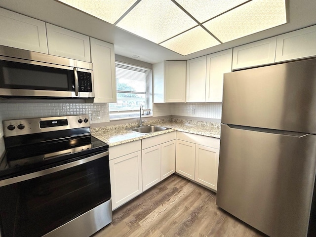 kitchen with appliances with stainless steel finishes, a sink, light wood-style floors, white cabinetry, and backsplash