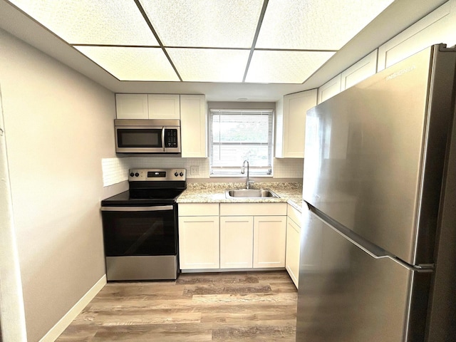 kitchen with a sink, stainless steel appliances, baseboards, light wood-type flooring, and backsplash