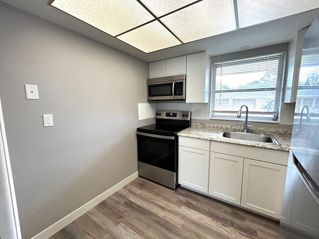 kitchen featuring appliances with stainless steel finishes, a sink, white cabinetry, baseboards, and wood finished floors