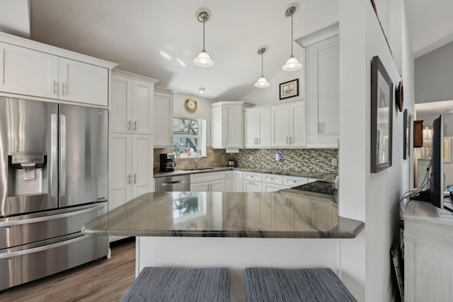 kitchen with a peninsula, white cabinets, tasteful backsplash, a sink, and stainless steel appliances