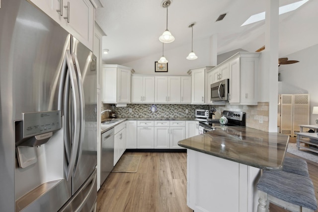kitchen featuring stainless steel appliances, tasteful backsplash, vaulted ceiling with skylight, and a peninsula