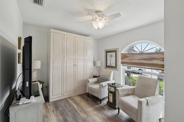 living area with a textured ceiling, a ceiling fan, wood finished floors, and visible vents