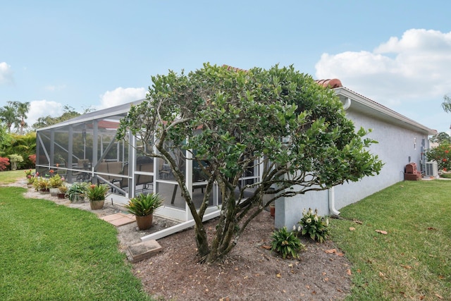 back of property with a lawn, a lanai, central AC unit, and stucco siding