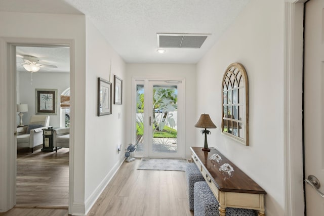 entryway with visible vents, baseboards, a textured ceiling, a ceiling fan, and light wood-style flooring