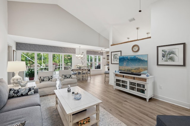 living area with high vaulted ceiling, a chandelier, baseboards, wood finished floors, and visible vents