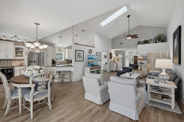 living room with beverage cooler, high vaulted ceiling, light wood finished floors, ceiling fan with notable chandelier, and a skylight