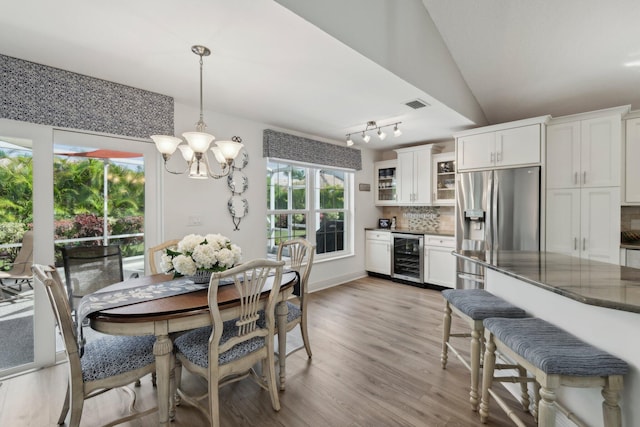 dining space featuring visible vents, wine cooler, light wood-style floors, a notable chandelier, and vaulted ceiling