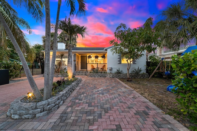 425 32nd St, West Palm Beach, FL 33407 - back of house at dusk with an outdoor fire pit, fence, stucco siding, and a porch