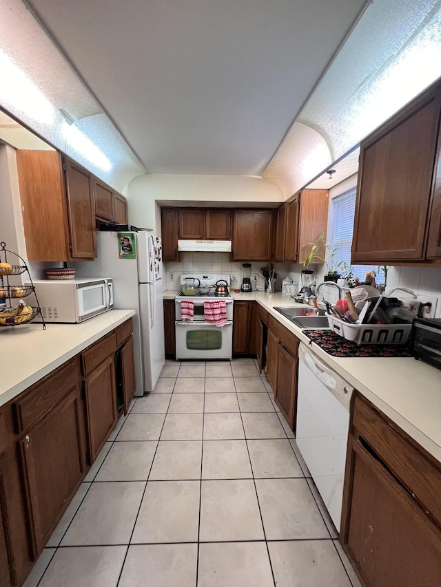 kitchen with white appliances, light tile patterned floors, under cabinet range hood, light countertops, and a sink