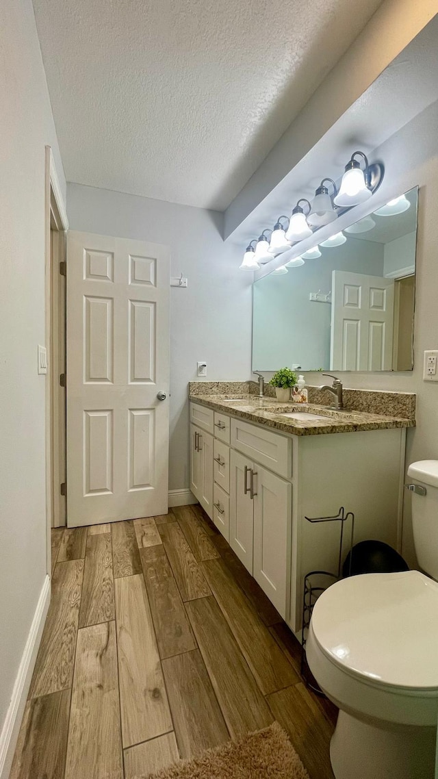 1044 Nin St, Orlando, FL 32835 - full bath featuring wood finished floors, toilet, double vanity, a textured ceiling, and baseboards