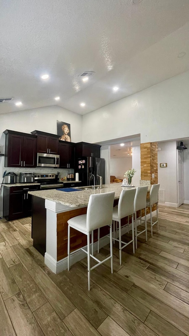 1044 Nin St, Orlando, FL 32835 - kitchen with stainless steel appliances, light wood-type flooring, a kitchen bar, vaulted ceiling, and light stone countertops