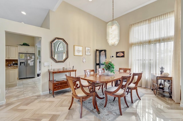 dining space featuring baseboards, high vaulted ceiling, and an inviting chandelier
