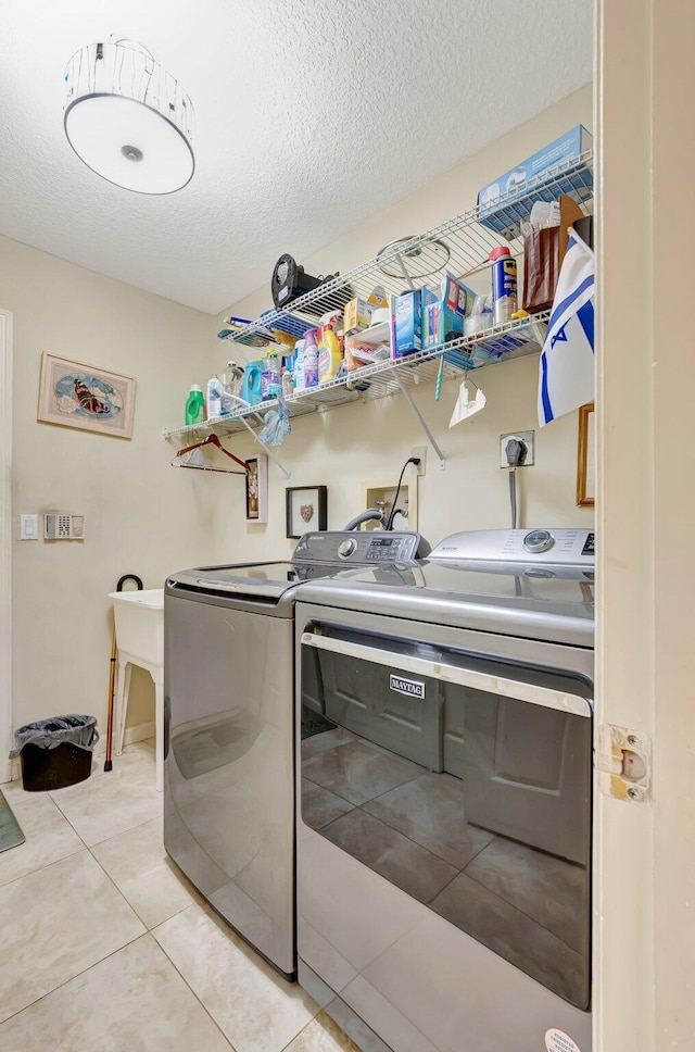 laundry room featuring separate washer and dryer, laundry area, a textured ceiling, and light tile patterned floors