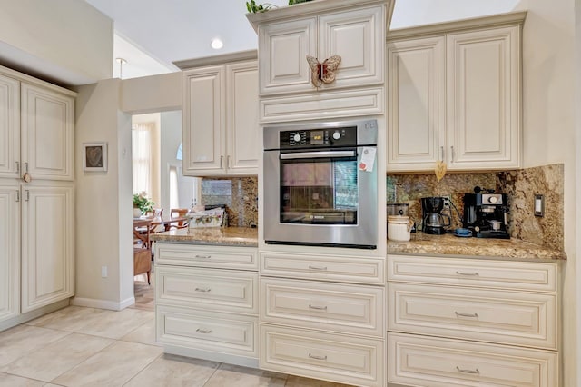 kitchen with backsplash, light tile patterned floors, cream cabinets, and oven