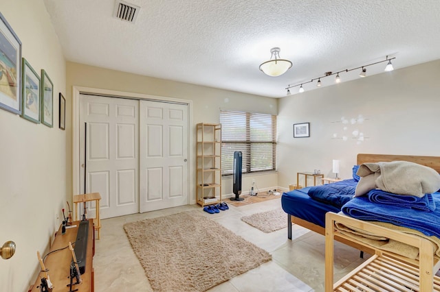 bedroom with a textured ceiling, visible vents, light tile patterned floors, and a closet