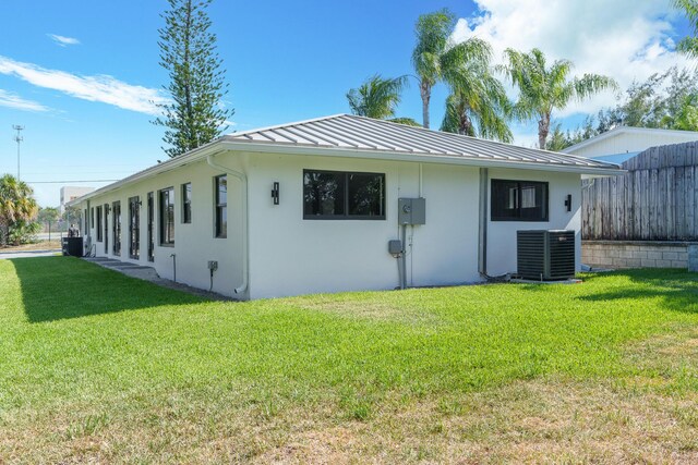 303/305 De Carie, Delray Beach, FL 33444 - view of side of property with fence, stucco siding, a standing seam roof, a lawn, and central air condition unit