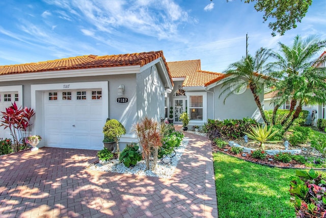 mediterranean / spanish-style house featuring decorative driveway, an attached garage, a tile roof, and stucco siding