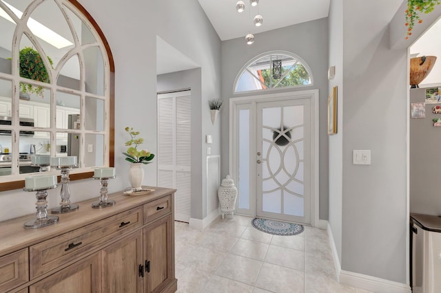entryway with baseboards, light tile patterned floors, and high vaulted ceiling
