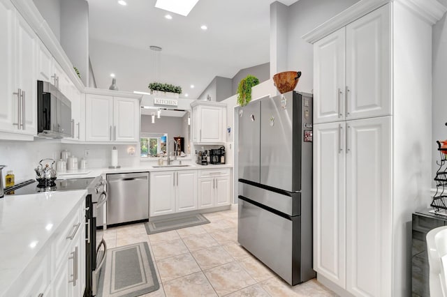 kitchen featuring white cabinets, appliances with stainless steel finishes, a sink, vaulted ceiling with skylight, and light countertops