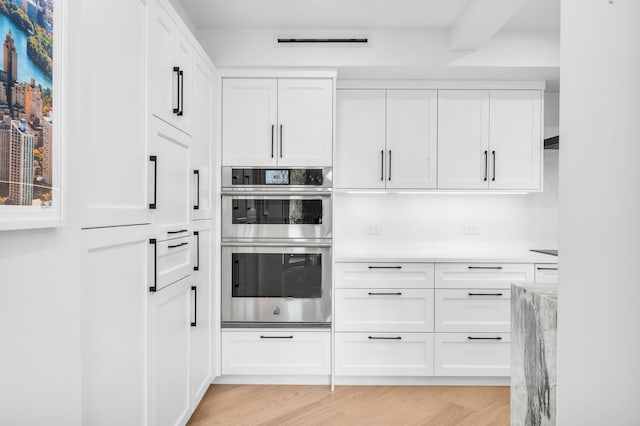 kitchen with light wood-style flooring, stainless steel double oven, white cabinetry, and light countertops