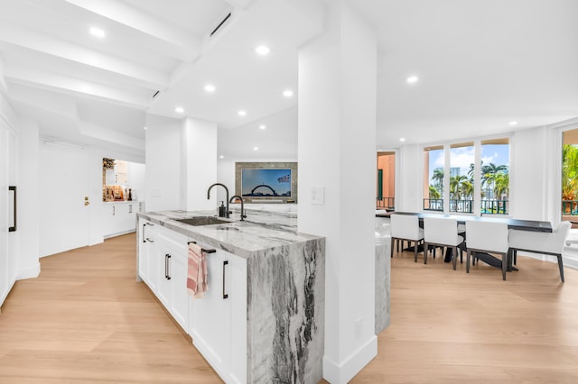 kitchen with recessed lighting, light wood-style flooring, light stone counters, white cabinets, and a sink