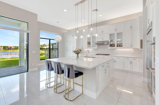 kitchen with glass insert cabinets, light countertops, under cabinet range hood, white cabinets, and a sink