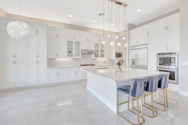 kitchen with a sink, light countertops, white cabinets, built in appliances, and under cabinet range hood