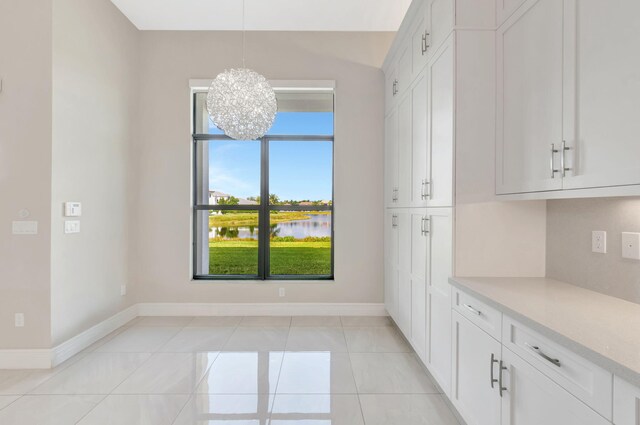 unfurnished dining area featuring baseboards, a water view, light tile patterned floors, and a chandelier