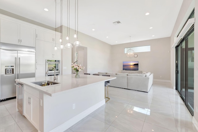 kitchen with white cabinets, light countertops, stainless steel appliances, a large island with sink, and visible vents
