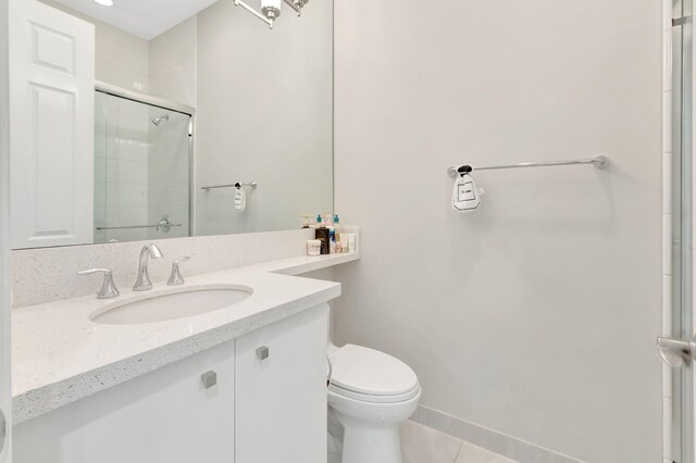 bathroom featuring tile patterned flooring, vanity, toilet, baseboards, and tiled shower