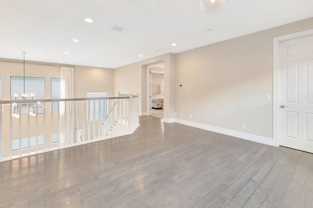 empty room with baseboards, recessed lighting, wood finished floors, and a notable chandelier