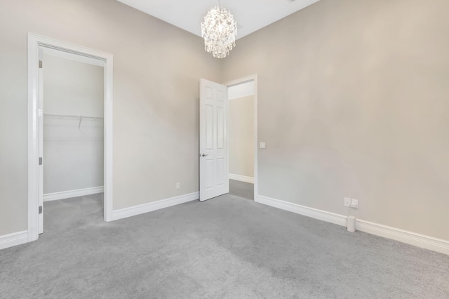 unfurnished bedroom featuring a walk in closet, baseboards, a closet, an inviting chandelier, and carpet flooring
