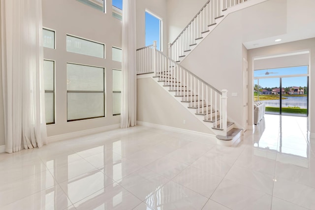 entryway with baseboards, tile patterned flooring, stairs, and a towering ceiling