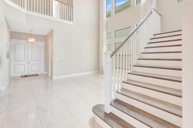 stairs featuring baseboards, tile patterned floors, a high ceiling, and a notable chandelier