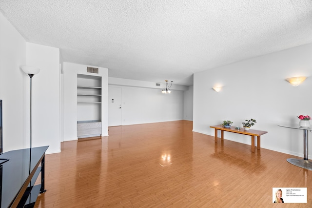 137 Golden Isles Dr Unit 806, Hallandale Beach, FL 33009 - unfurnished living room featuring a textured ceiling, wood finished floors, built in shelves, and a chandelier